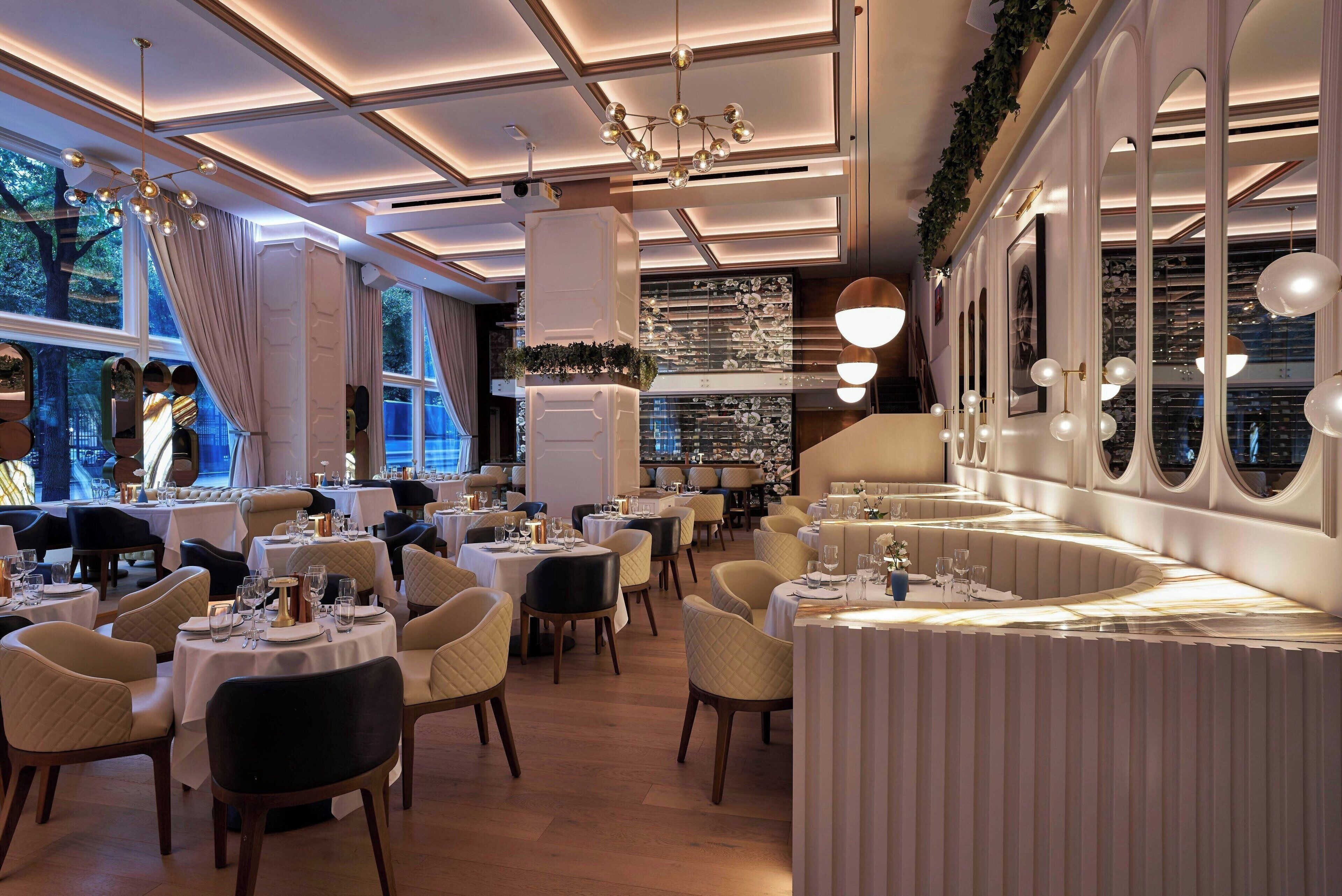 Un restaurante con mesas redondas, sillas y una zona de bar.