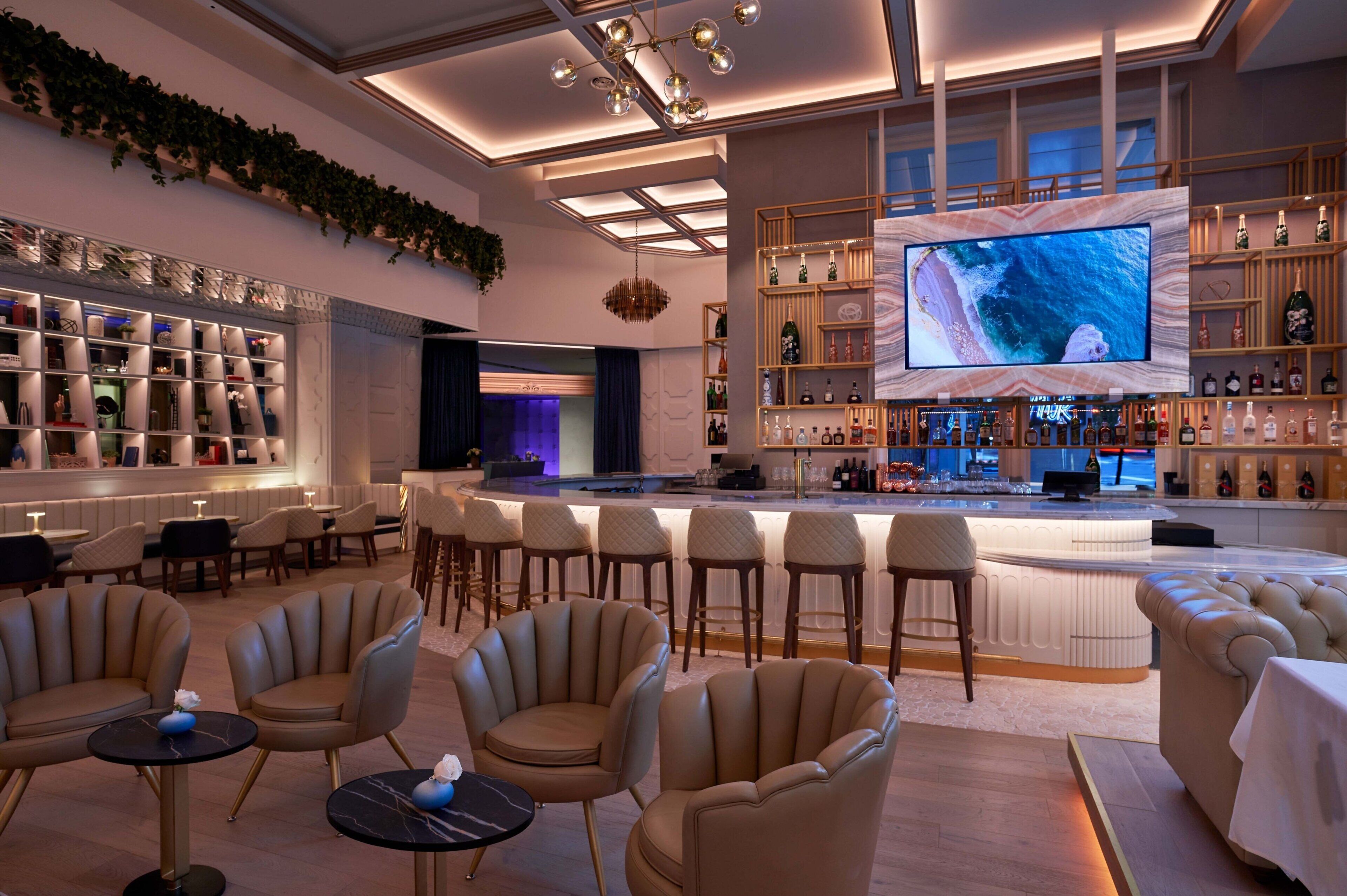 A modern bar area with a large TV screen, comfortable seating, and a well-stocked liquor shelf.