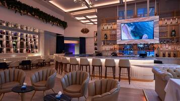 A modern bar area with a large TV screen, comfortable seating, and a well-stocked liquor shelf.