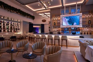 Angolo bar moderno con un grande schermo televisivo, sedute confortevoli e un'ampia selezione di liquori.