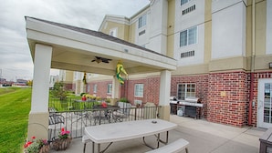 An outdoor patio area with a covered seating area, a grill, and potted plants.
