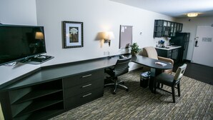 A compact hotel room with a kitchenette, a desk with a chair, a television, and a framed picture on the wall.