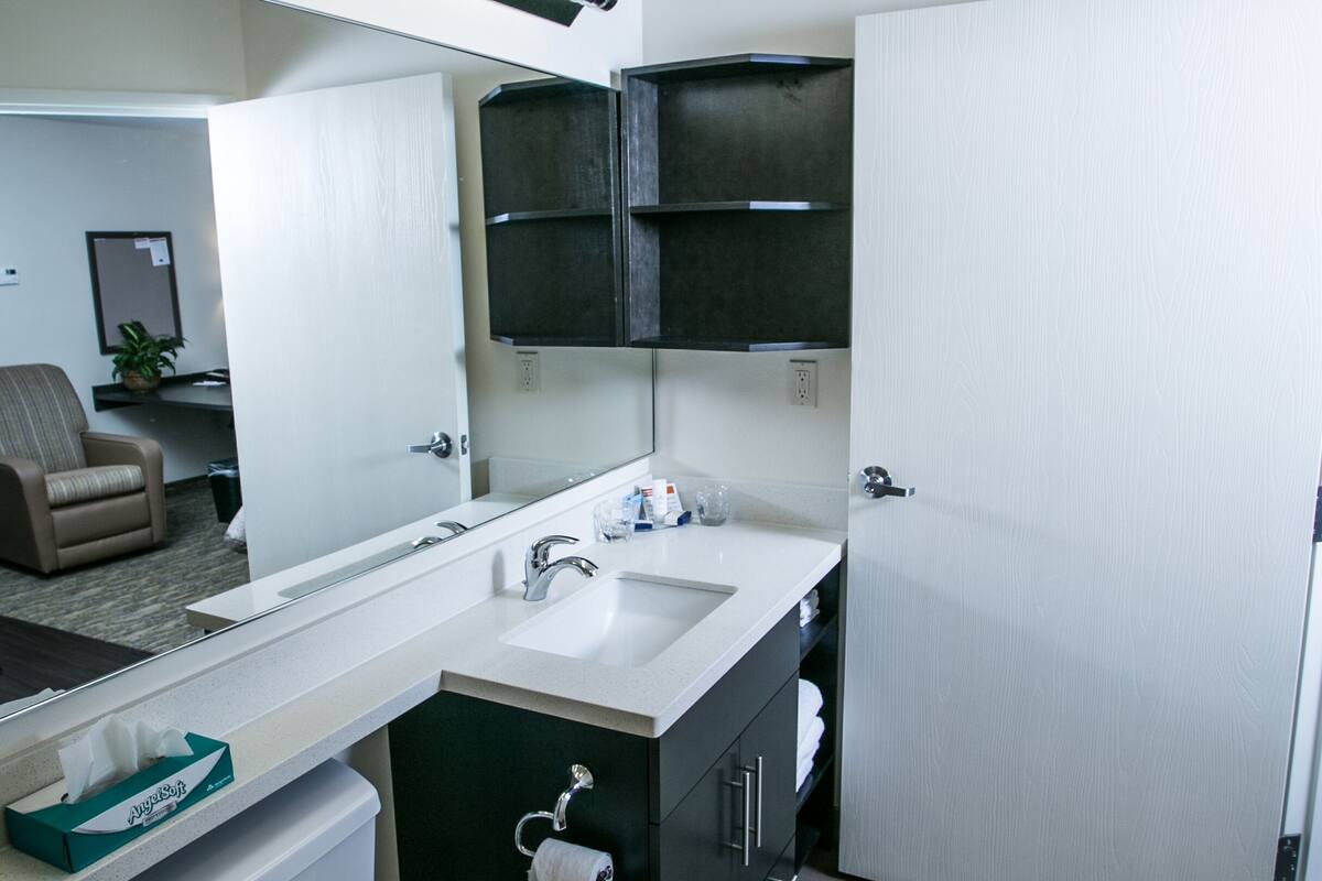 Een moderne badkamer met toilet, wastafel en spiegel. In de aangrenzende kamer staat een stoel en een plant.