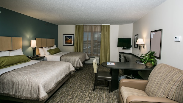 A hotel room with two beds, a desk, a chair, a sofa, a TV, and a window with curtains.