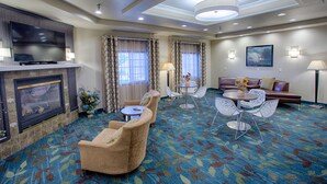 A hotel room with a flat-screen TV, a fireplace, a sofa, a dining table with chairs, and a patterned carpet.