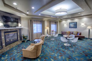 Habitación de hotel con televisión de pantalla plana, chimenea, sofá, mesa de comedor con sillas y alfombra estampada.