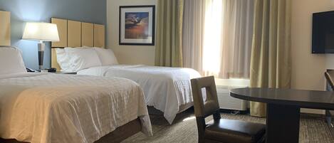 A hotel room with two beds, a desk, a chair, a lamp, a picture on the wall, and a television.