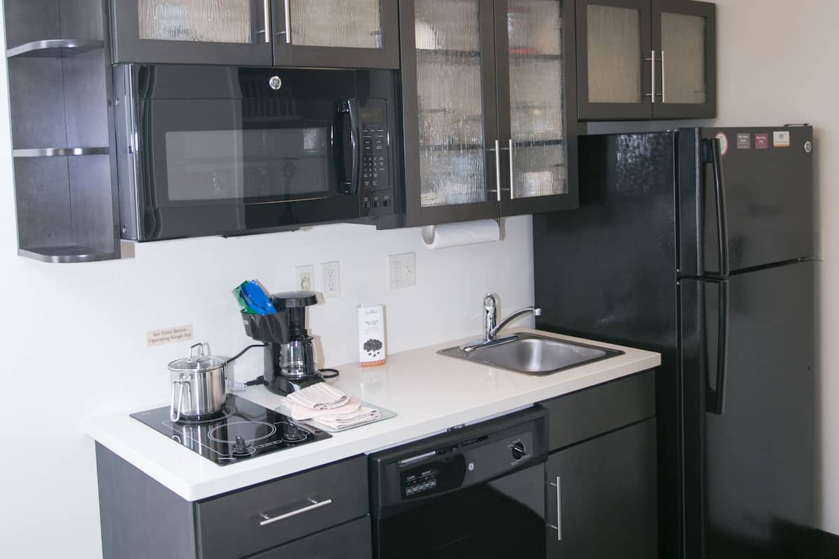 Een moderne keuken met donkere kastjes, een zwarte koelkast, een magnetron en een koffiezetapparaat.
