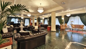 Een ruime lobby met leren banken, een weelderige kroonluchter en een piano.