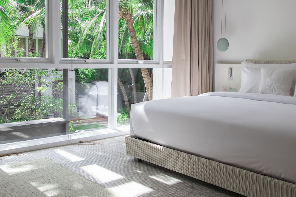 A bedroom with a large window, a bed, and a view of greenery outside.