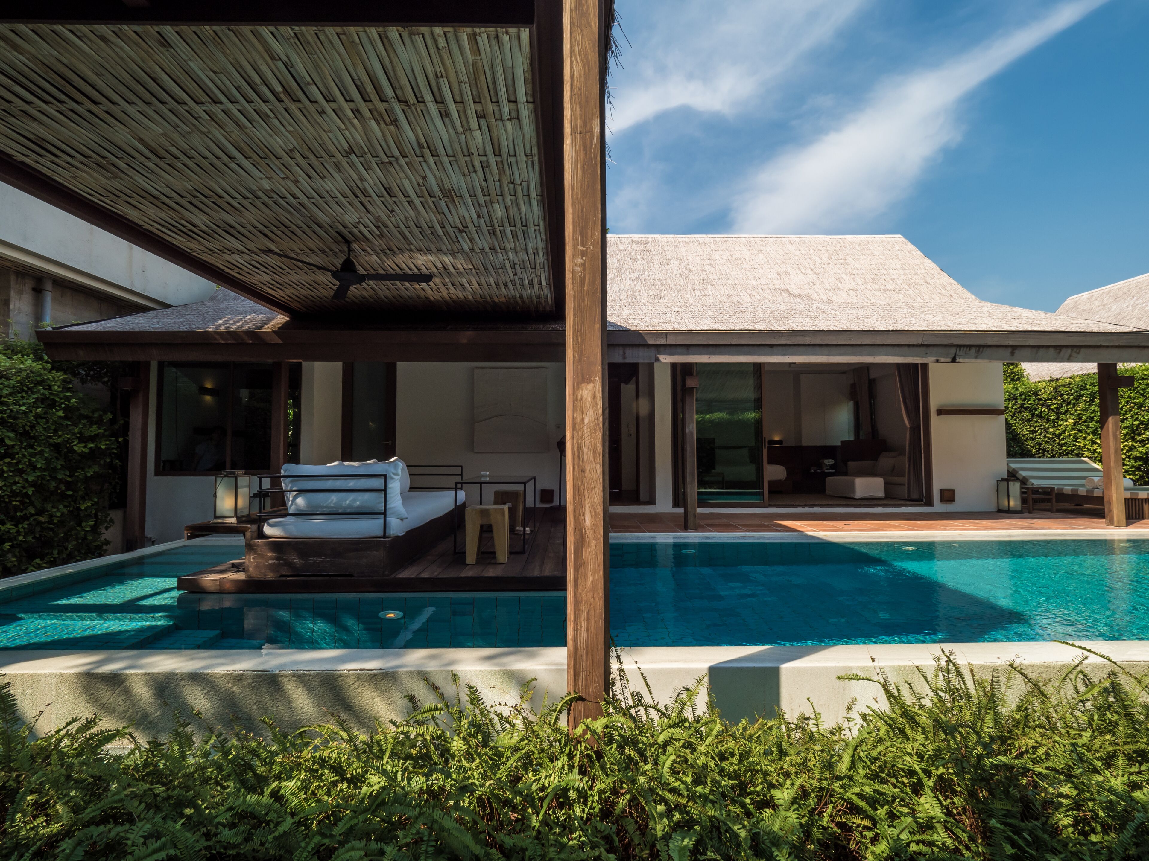 Een modern huis met een zwembad, een overdekt terras en een groot raam met uitzicht op het zwembad.