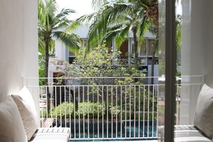 A balcony with white railings, a pool, and palm trees in the background.