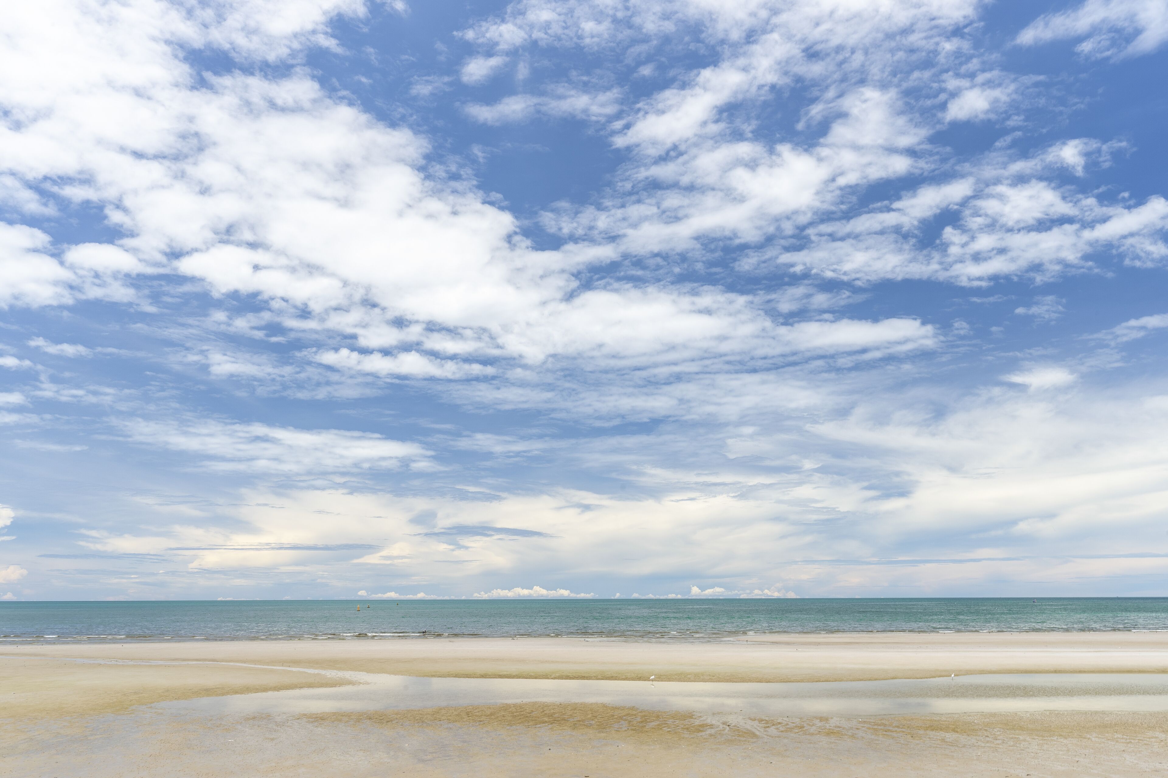 A beach with a wide sandy shore and a clear sky with scattered clouds.