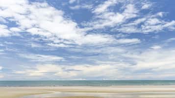 A beach with a wide sandy shore and a clear sky with scattered clouds.