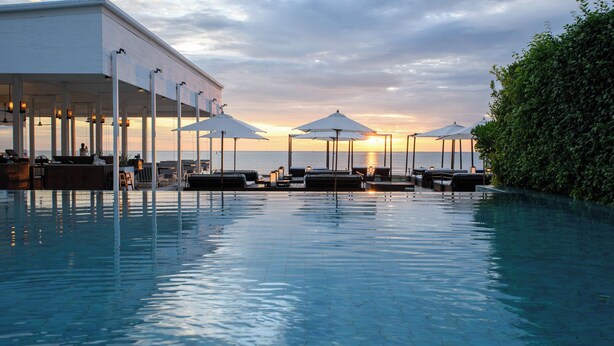 An infinity pool with lounge chairs and umbrellas, overlooking the sea.