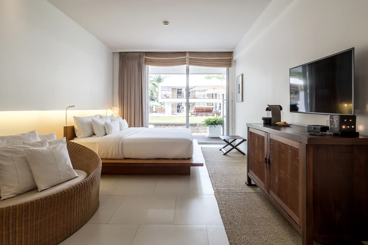A modern hotel room with a large bed, a television, a wicker sofa, and a view of the outside.