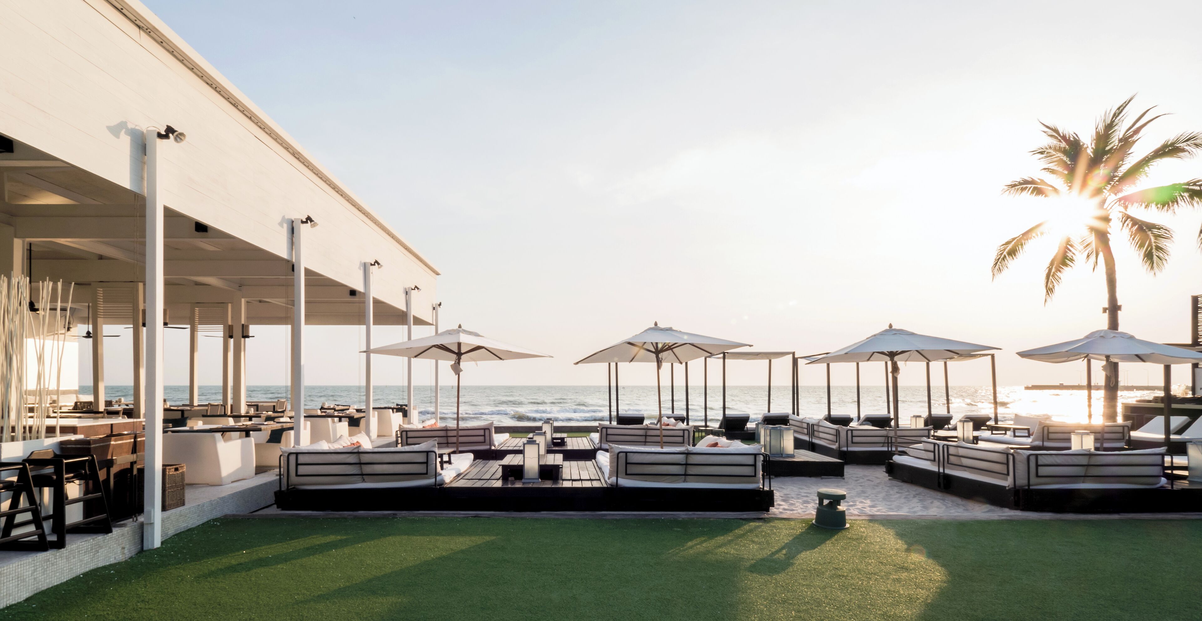 A beachside lounge area with outdoor seating and umbrellas, overlooking the ocean.