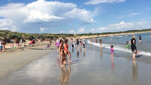 Una playa con gente caminando y parada en la arena, y el océano al fondo.