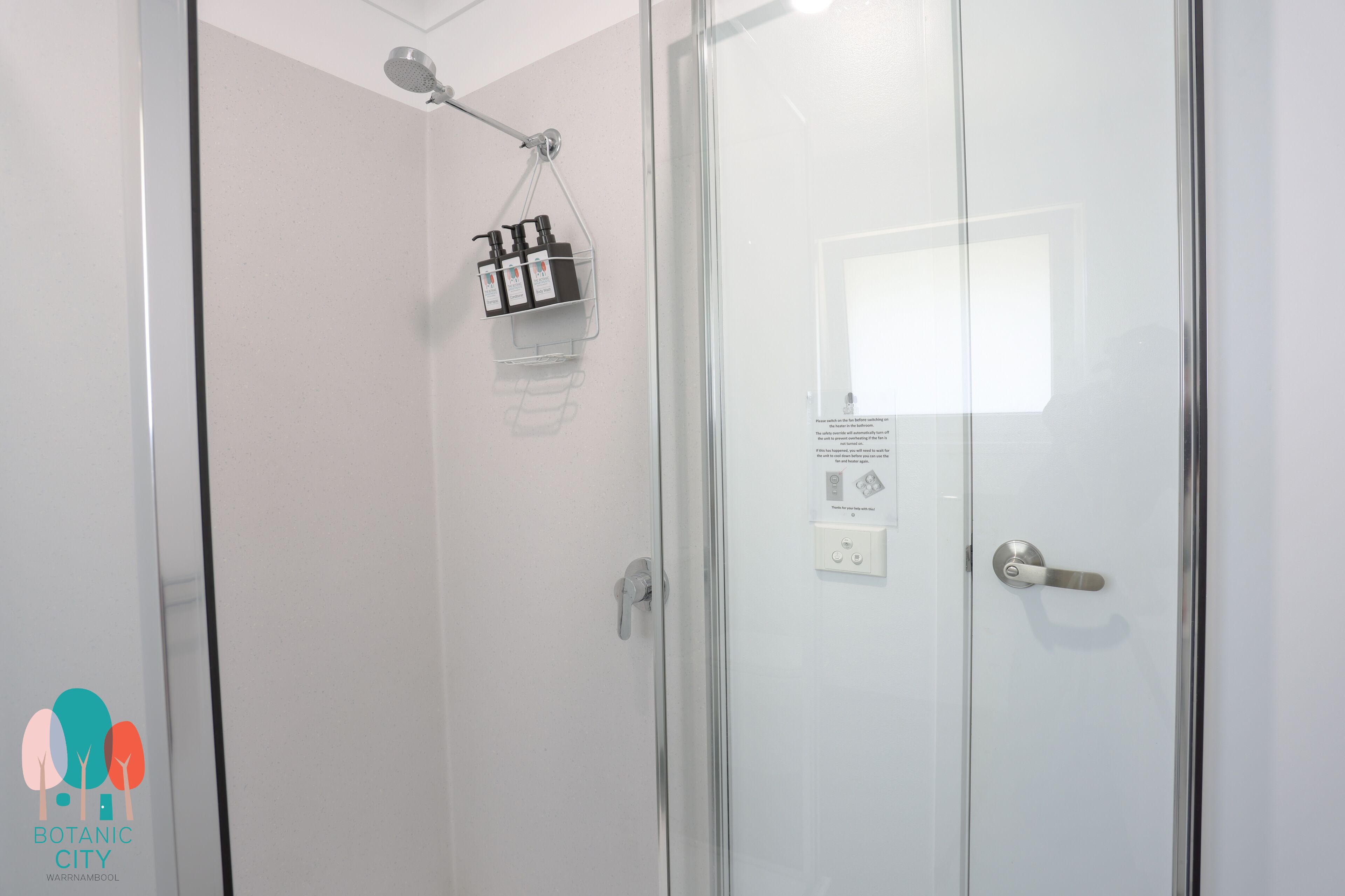 Un bagno moderno con cabina doccia in vetro, una porta bianca con maniglia e un piccolo ripiano con articoli da toilette.