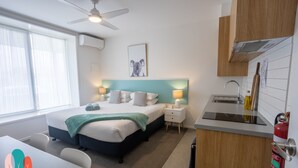 Una habitación de hotel moderna con cama, mesitas de noche, escritorio, kitchenette y ventilador de techo.