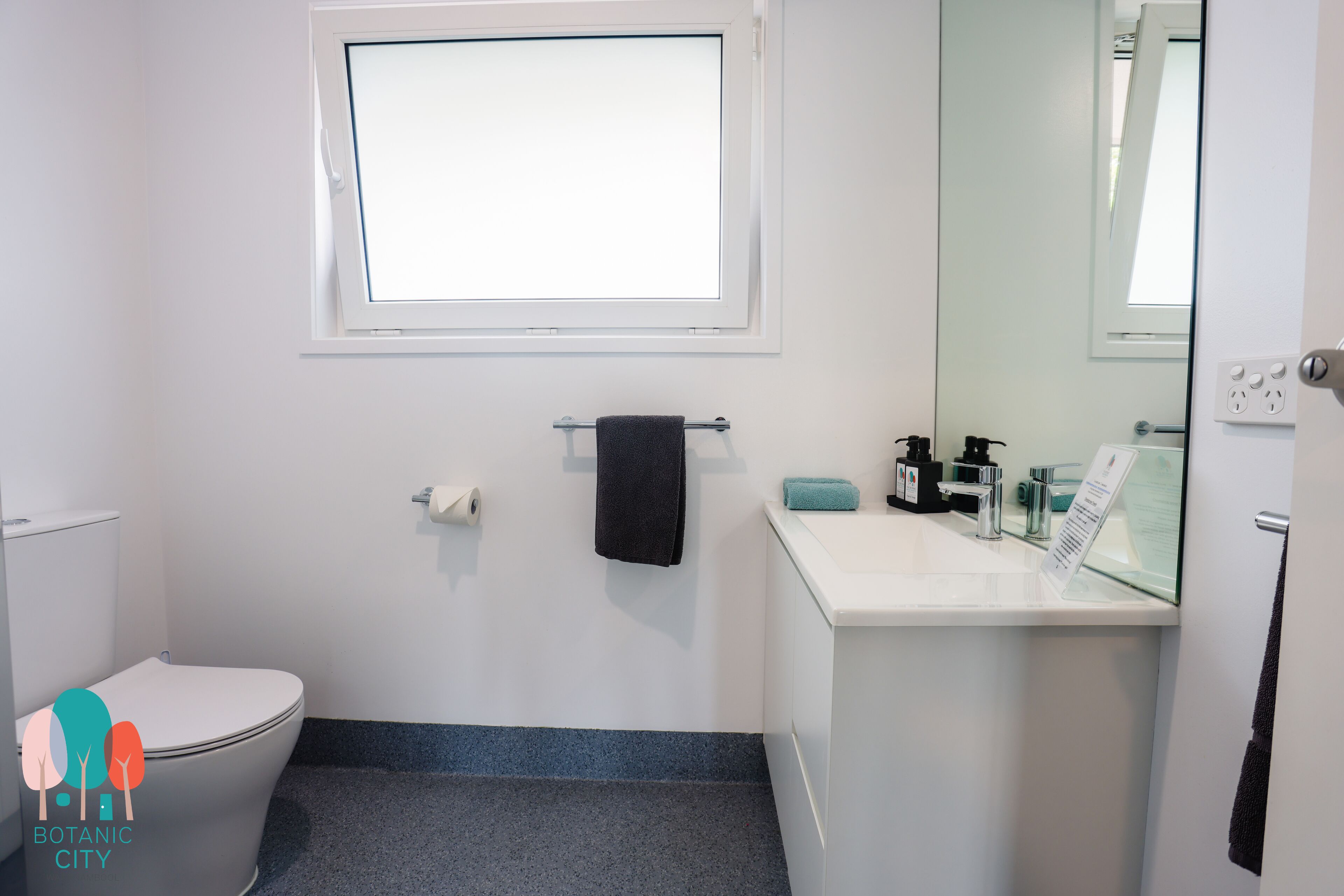 A bathroom with a toilet, a sink, a mirror, a towel rack, and a window.