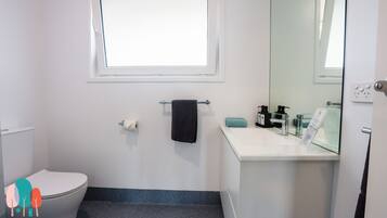 A bathroom with a toilet, a sink, a mirror, a towel rack, and a window.