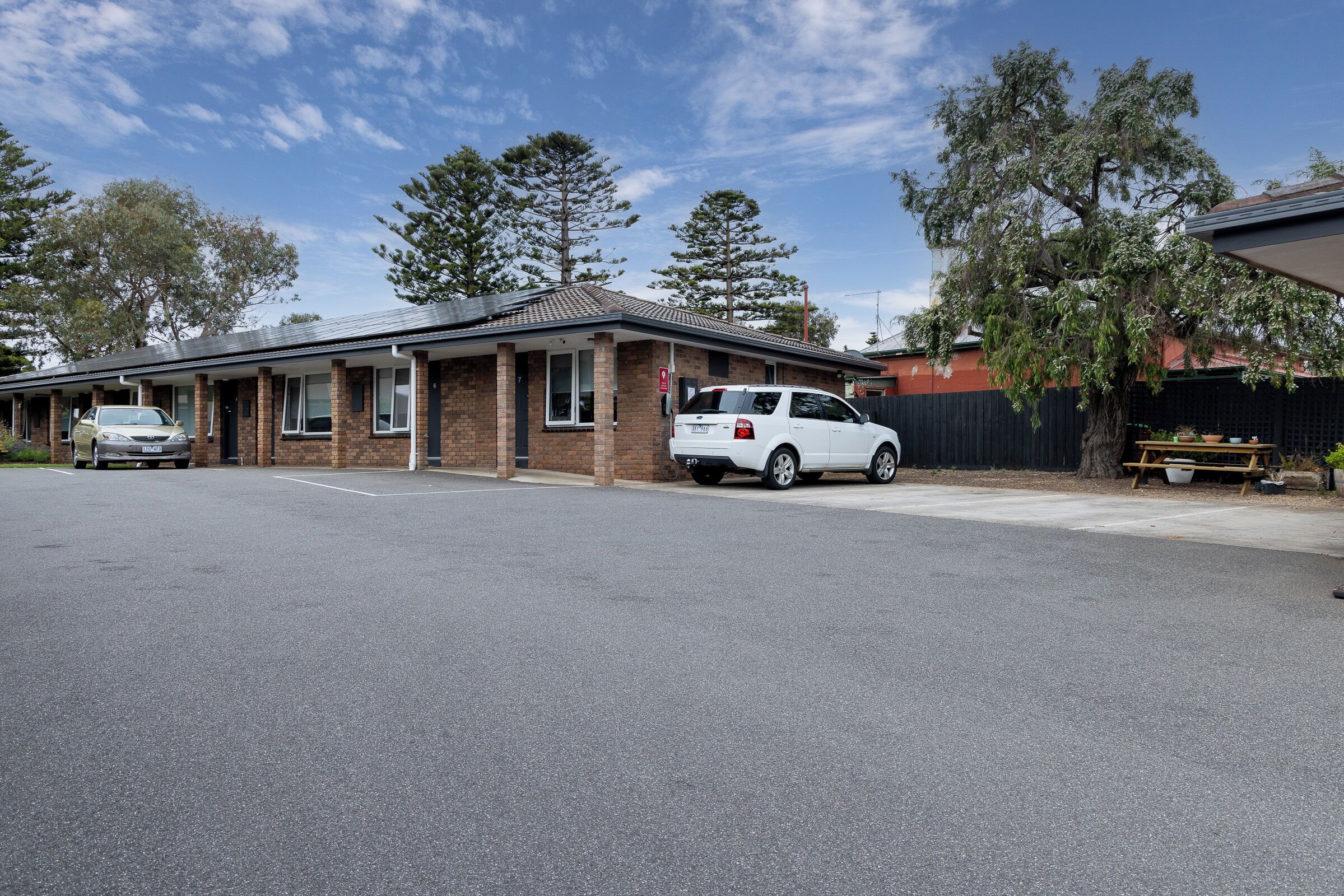 A single-story building with a brick facade, a carport, and a fenced yard.