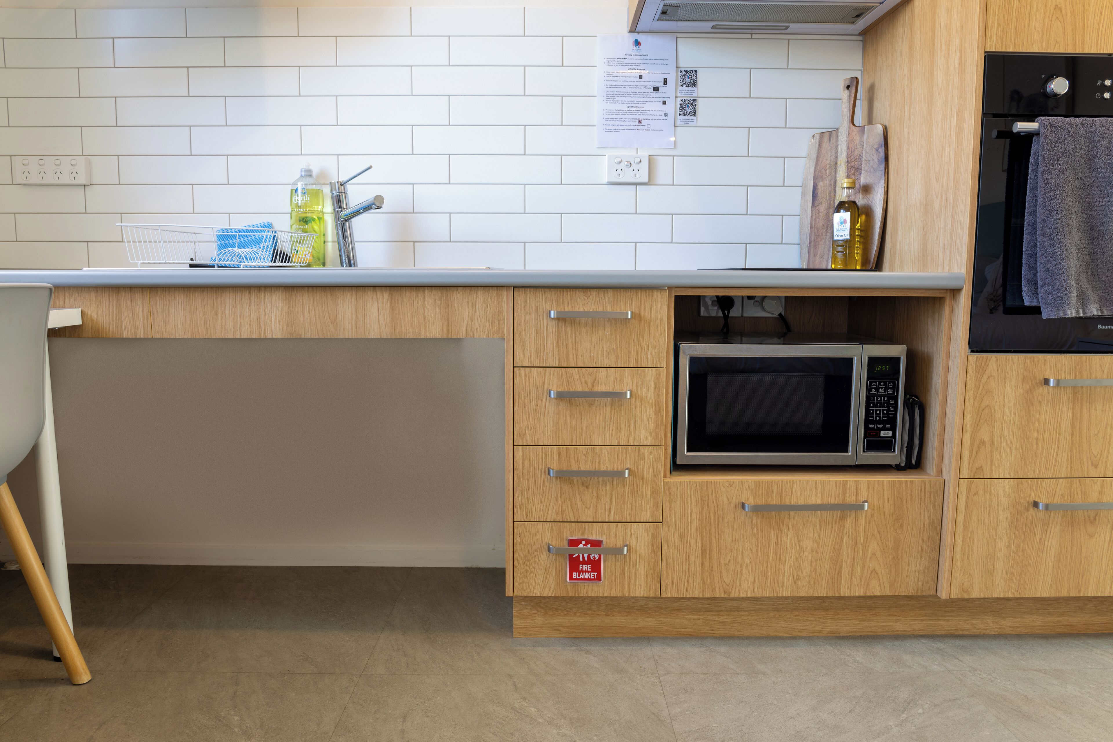 Ett kök med mikrovågsugn, träskåp, en diskho och en skylt som visar var brandfilten finns.
