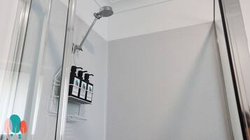 Un espace douche fermé par des parois de verre, doté d’un pommeau de douche à main et d’un distributeur de savon fixé au mur.