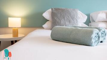 A neatly made bed with a rolled-up towel, a bedside lamp, and pillows against a teal wall.