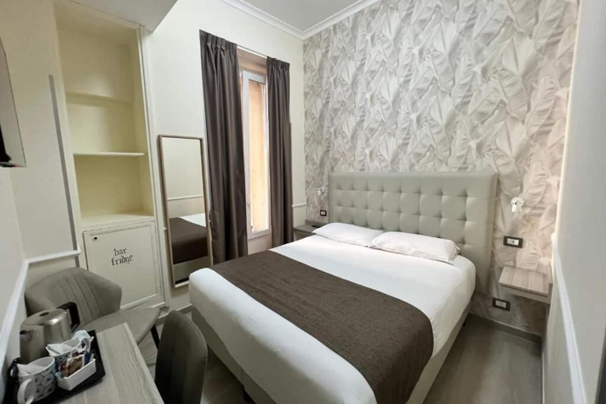 Una habitación de hotel con una cama grande, una mesita de noche, una silla, un espejo y un armario.