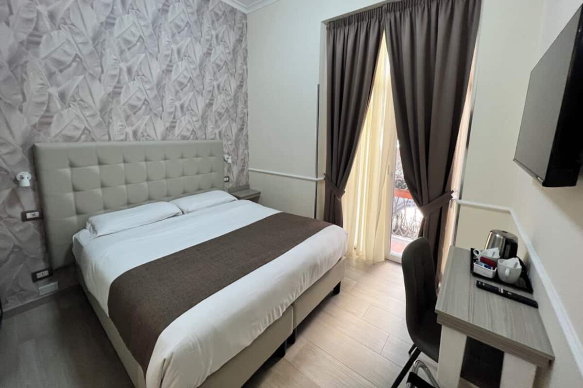 Habitación de hotel con una cama grande, un escritorio con silla, televisor y ventana con cortinas.