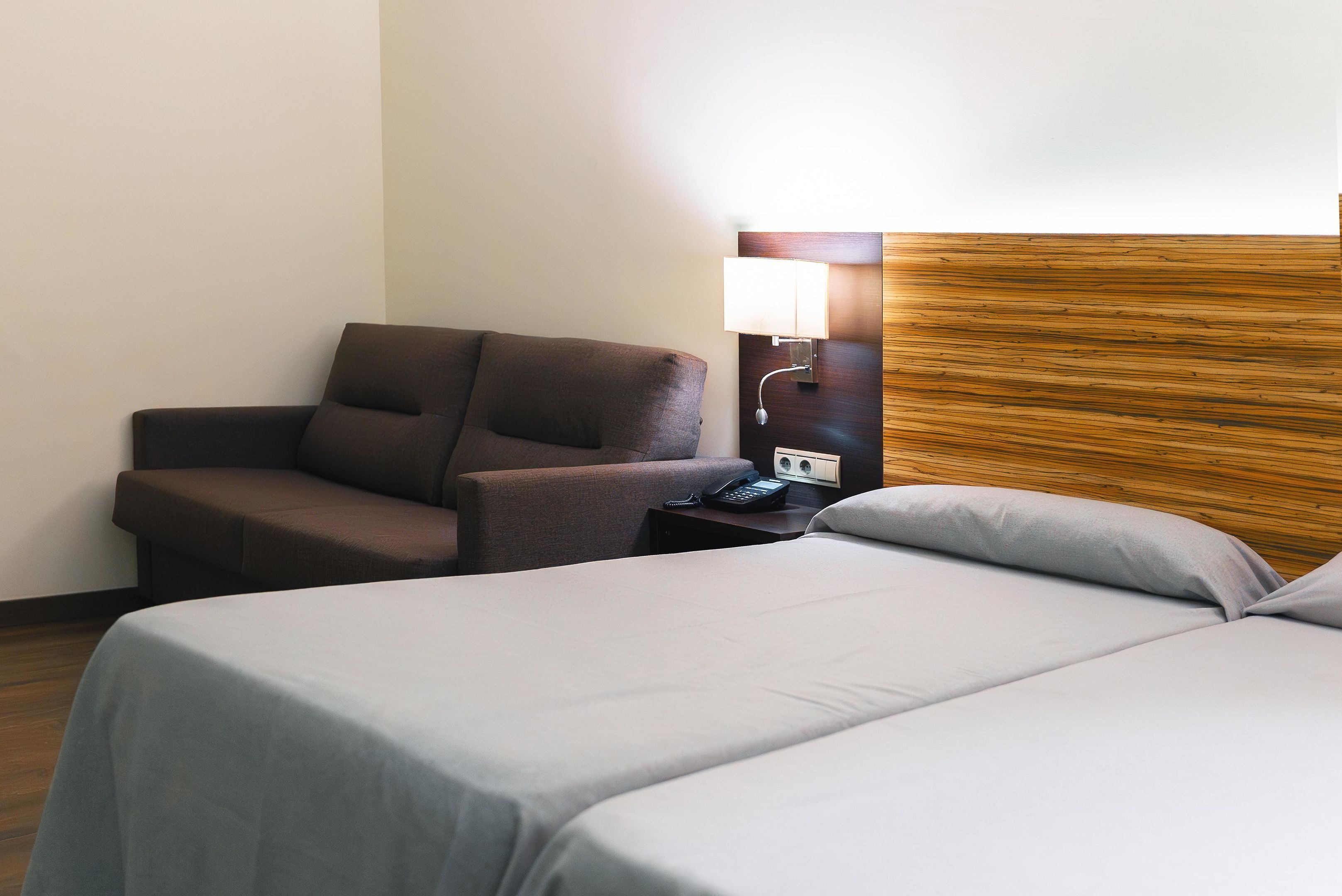 Une chambre d’hôtel avec un lit, une chaise, une table de chevet avec une lampe et une tête de lit en bois.