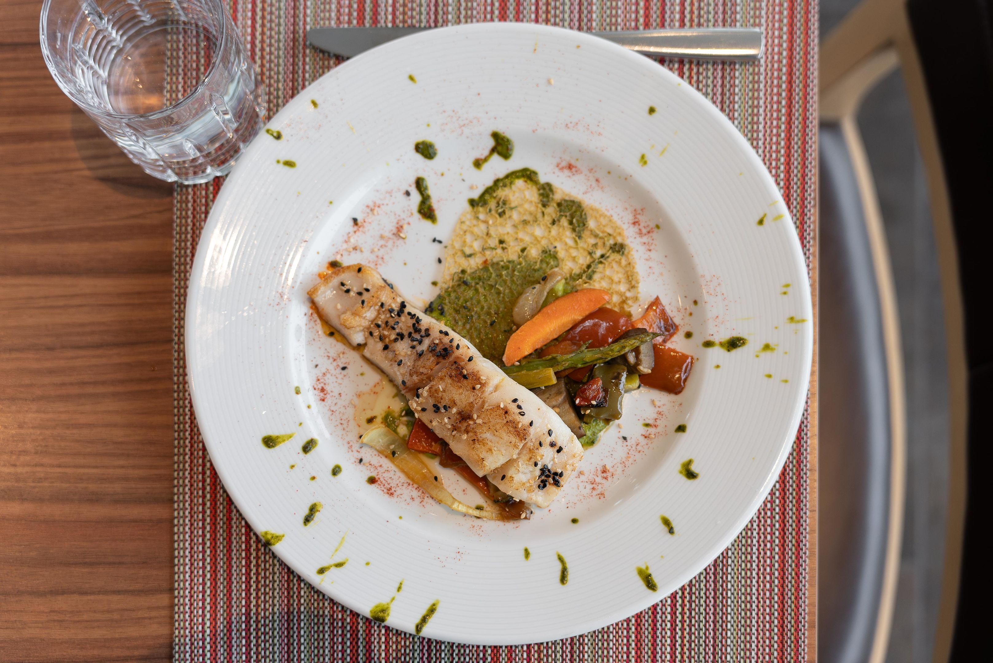 A plate with a rolled fish fillet, vegetables, and a green sauce on a white plate.