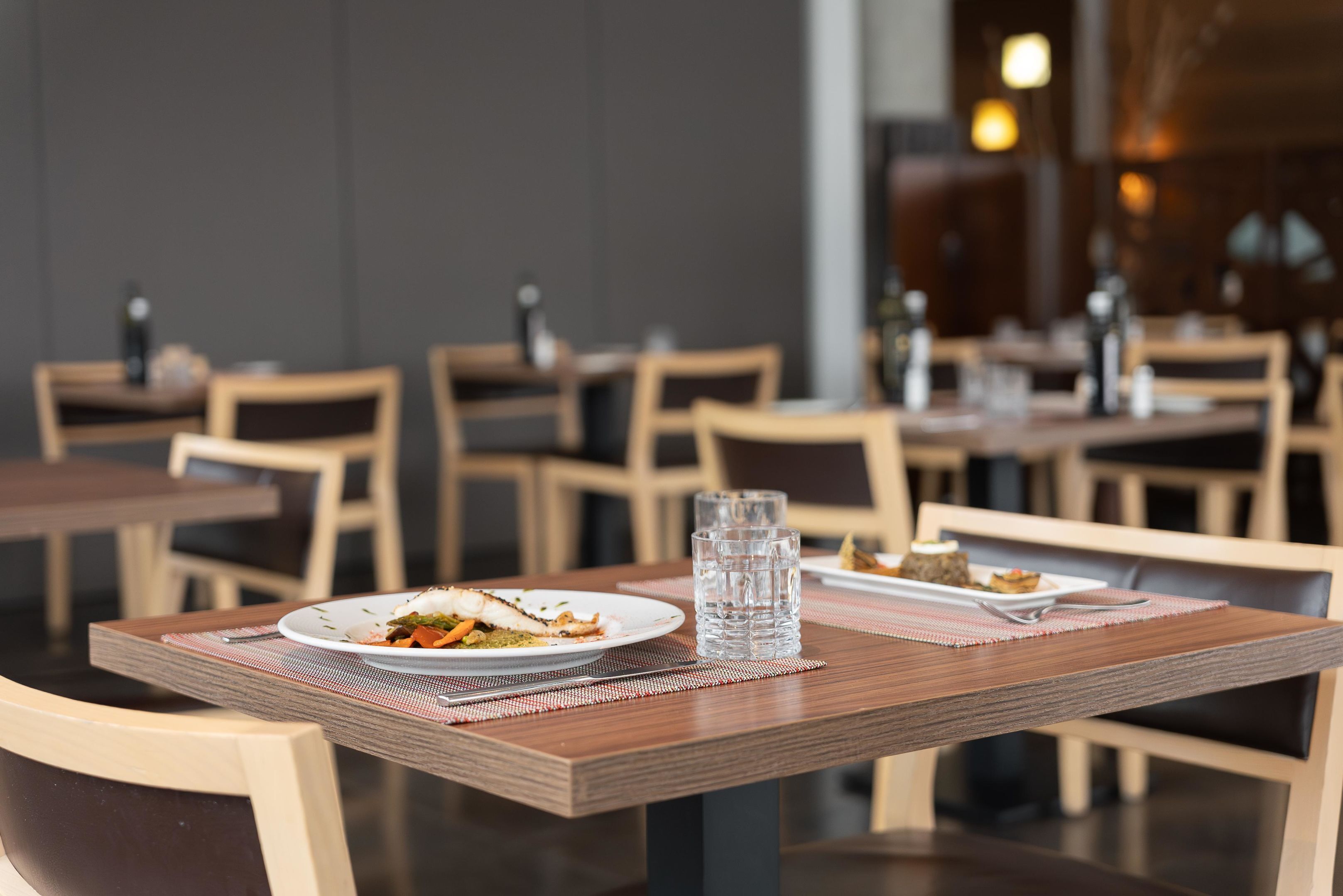 Een restaurant met houten tafels en stoelen, een waterglas op een onderzetter, en borden met eten.