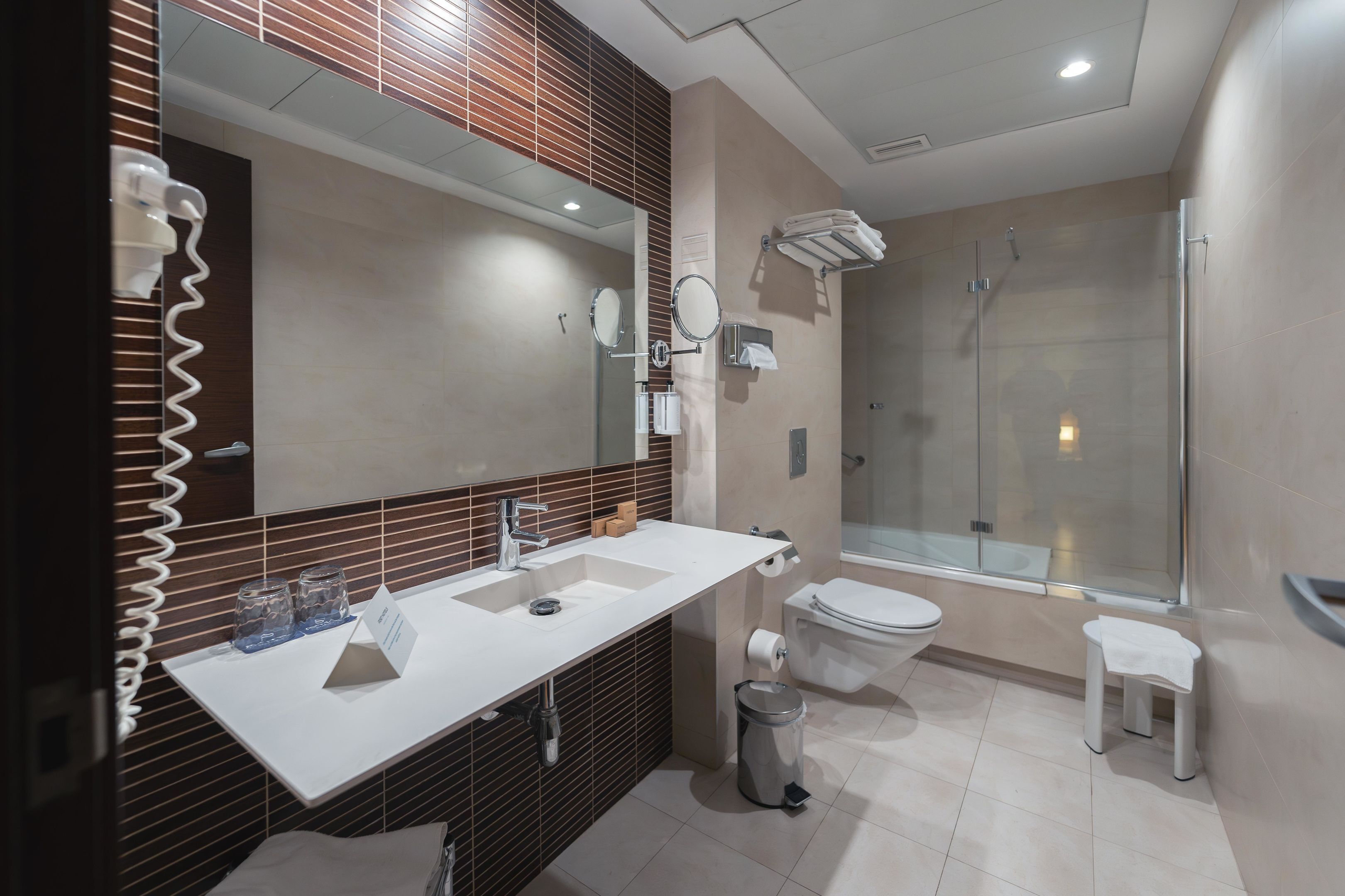 Un baño moderno con un espejo grande, dos lavamanos, inodoro y ducha con mampara de vidrio.
