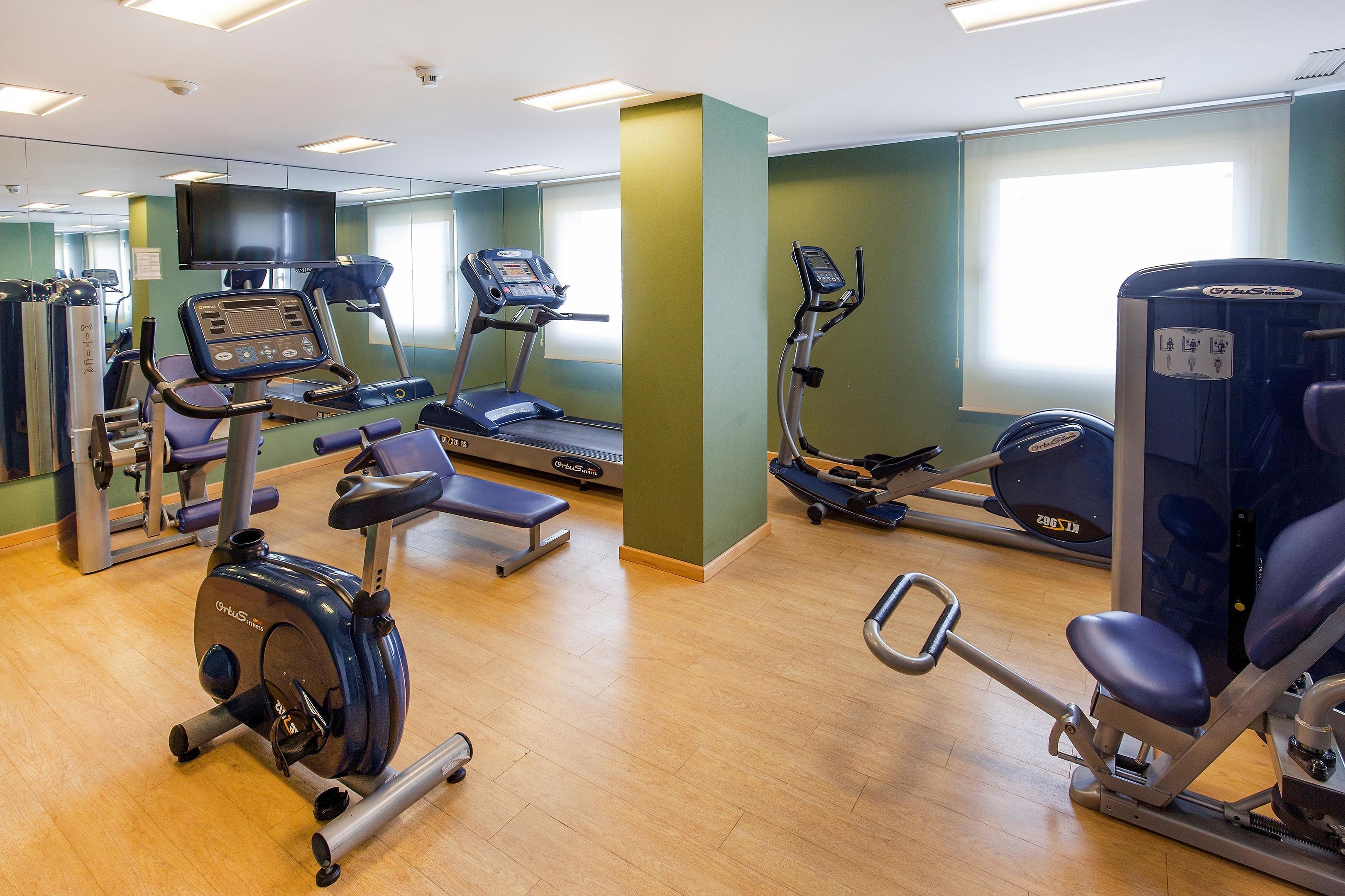 Un gimnasio con diversos equipos de ejercicio, incluyendo cintas de correr, elípticas y máquinas de pesas.