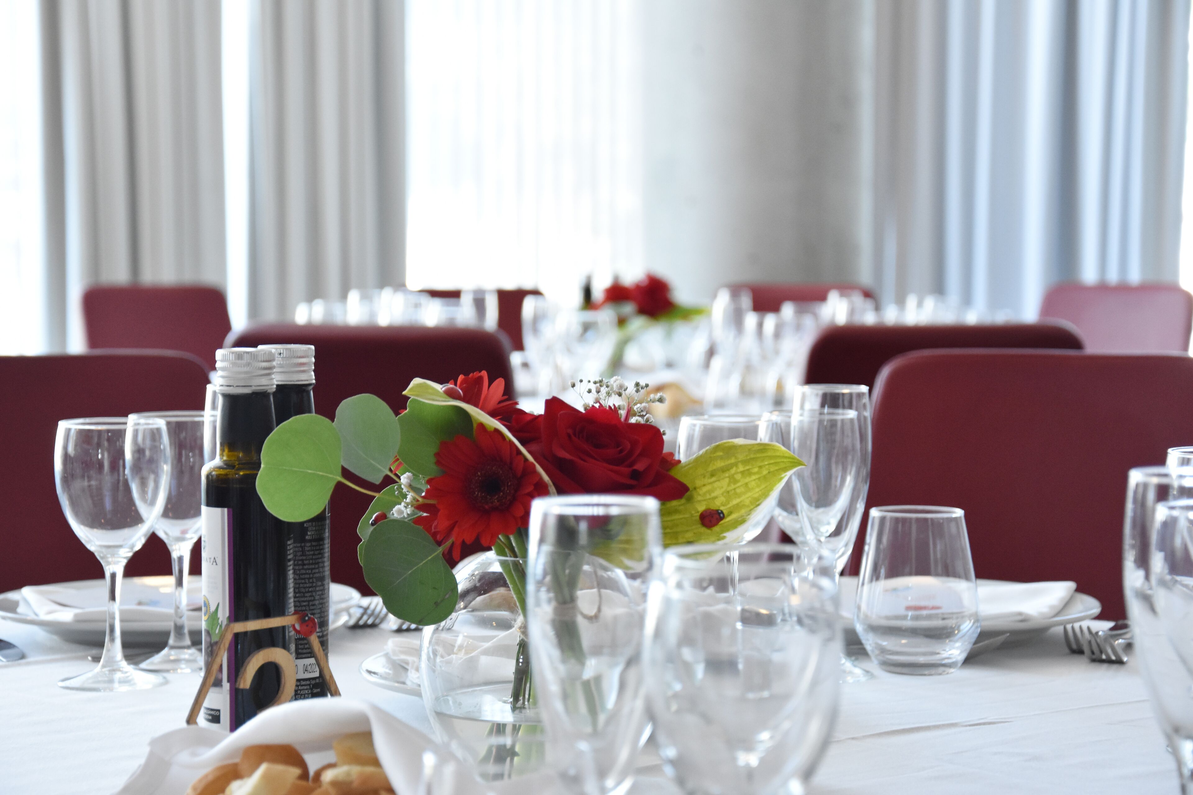 A dining table set with wine glasses, a bottle of wine, and red flowers.