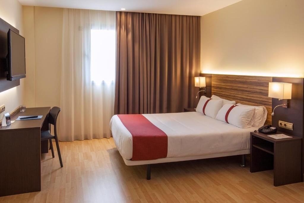 A hotel room with a bed, bedside tables, a desk, and a TV.