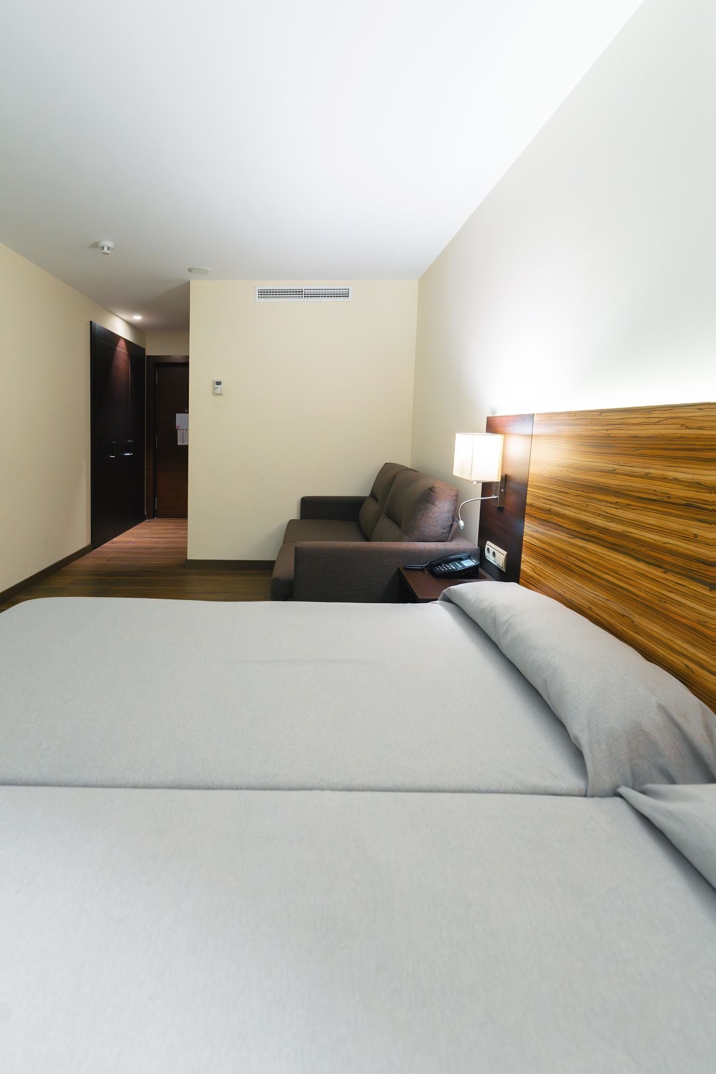 A hotel room with a bed, a sofa, a desk with a lamp, and a wooden headboard.