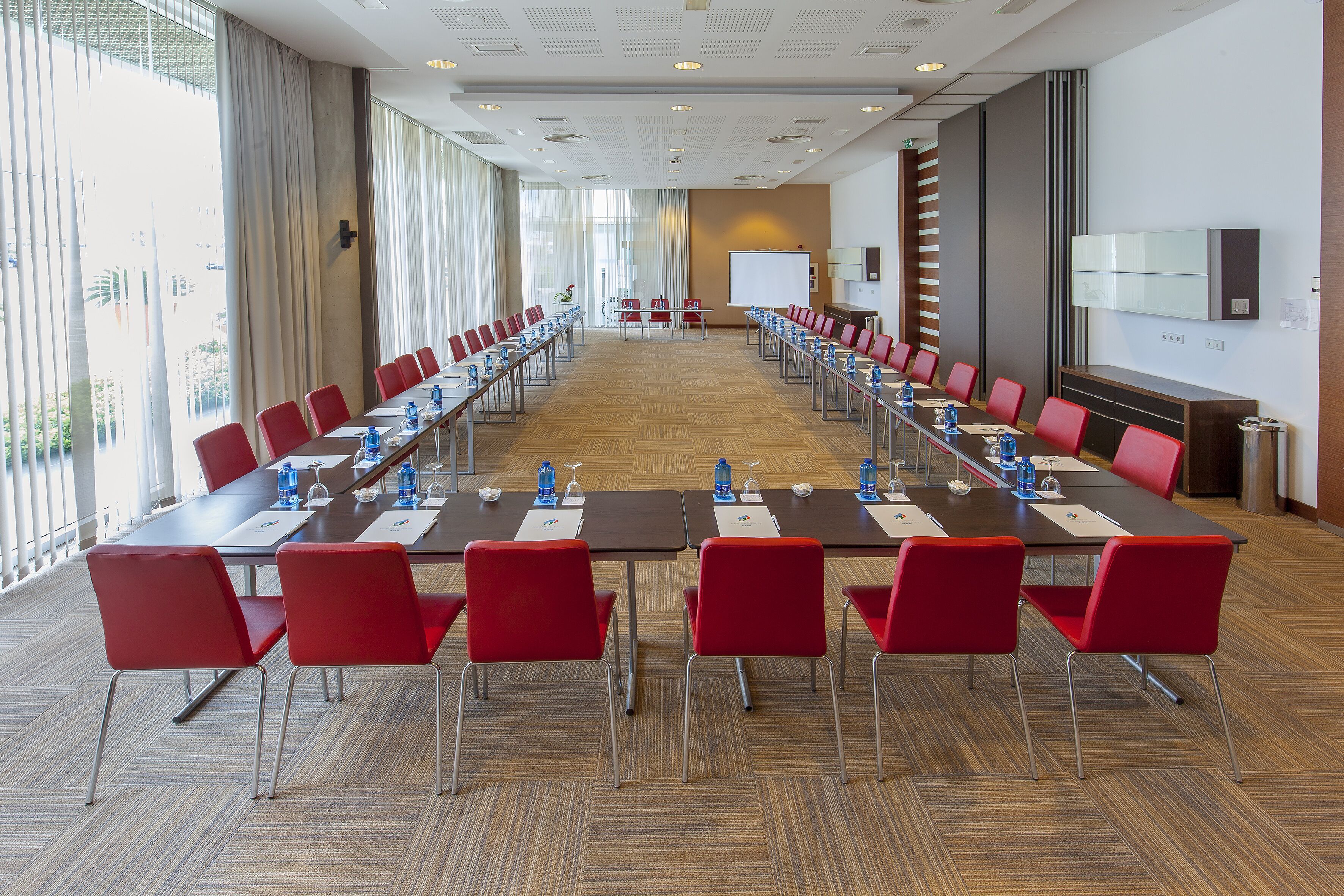 Une salle de conférence avec une longue table, des chaises rouges et un tableau blanc.