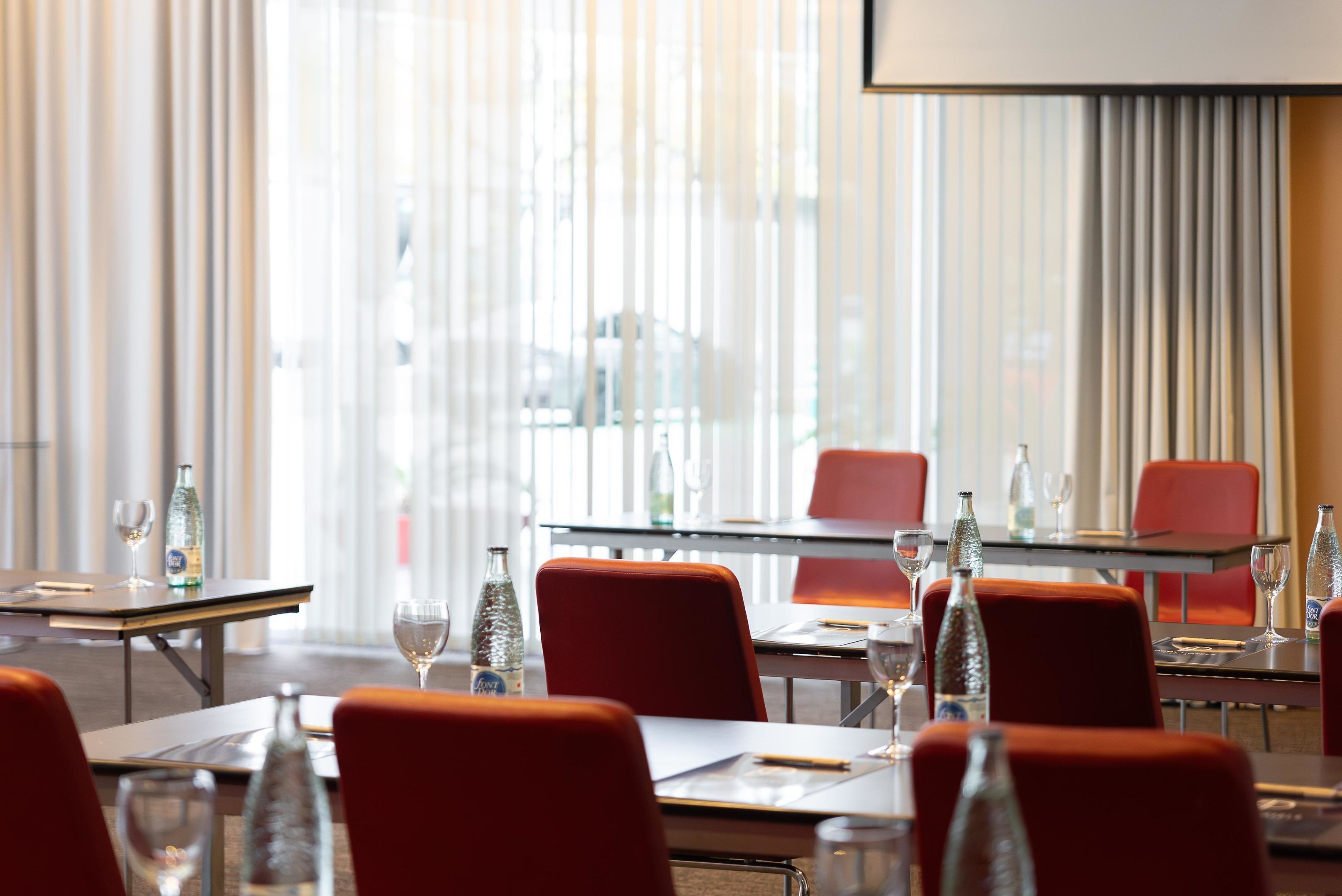 A conference room with glass tables, red chairs, and wine glasses.