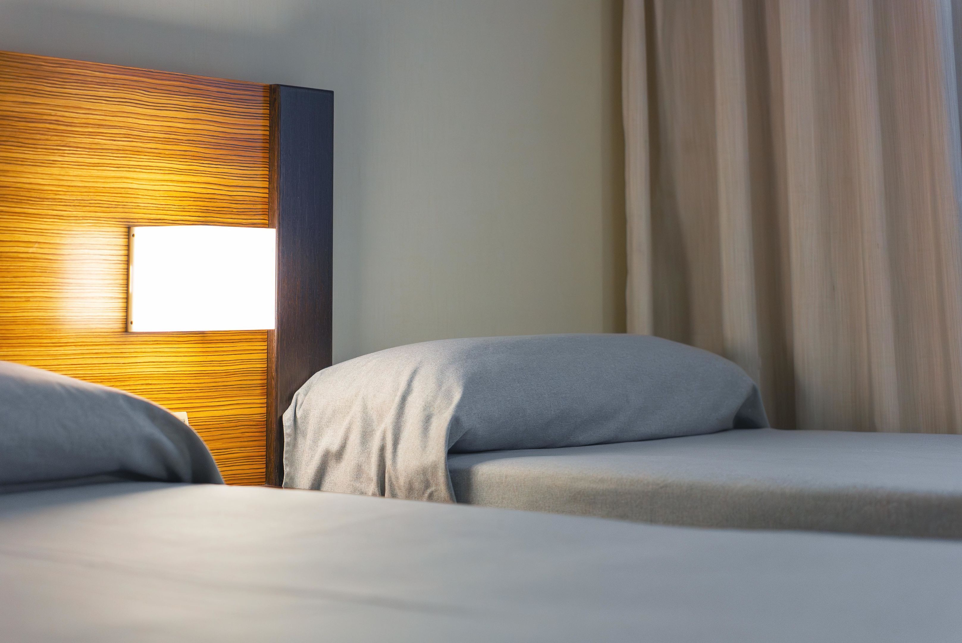 A hotel room with a wooden headboard, a bedside lamp, and two beds with grey bedding.