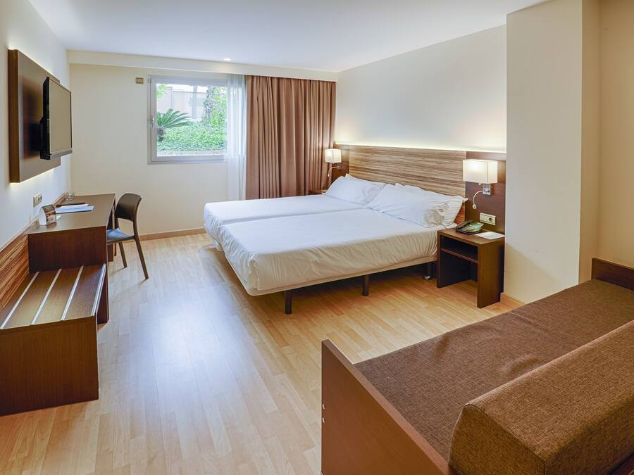 Habitación de hotel con cama, escritorio, silla, televisión y ventana con cortinas.