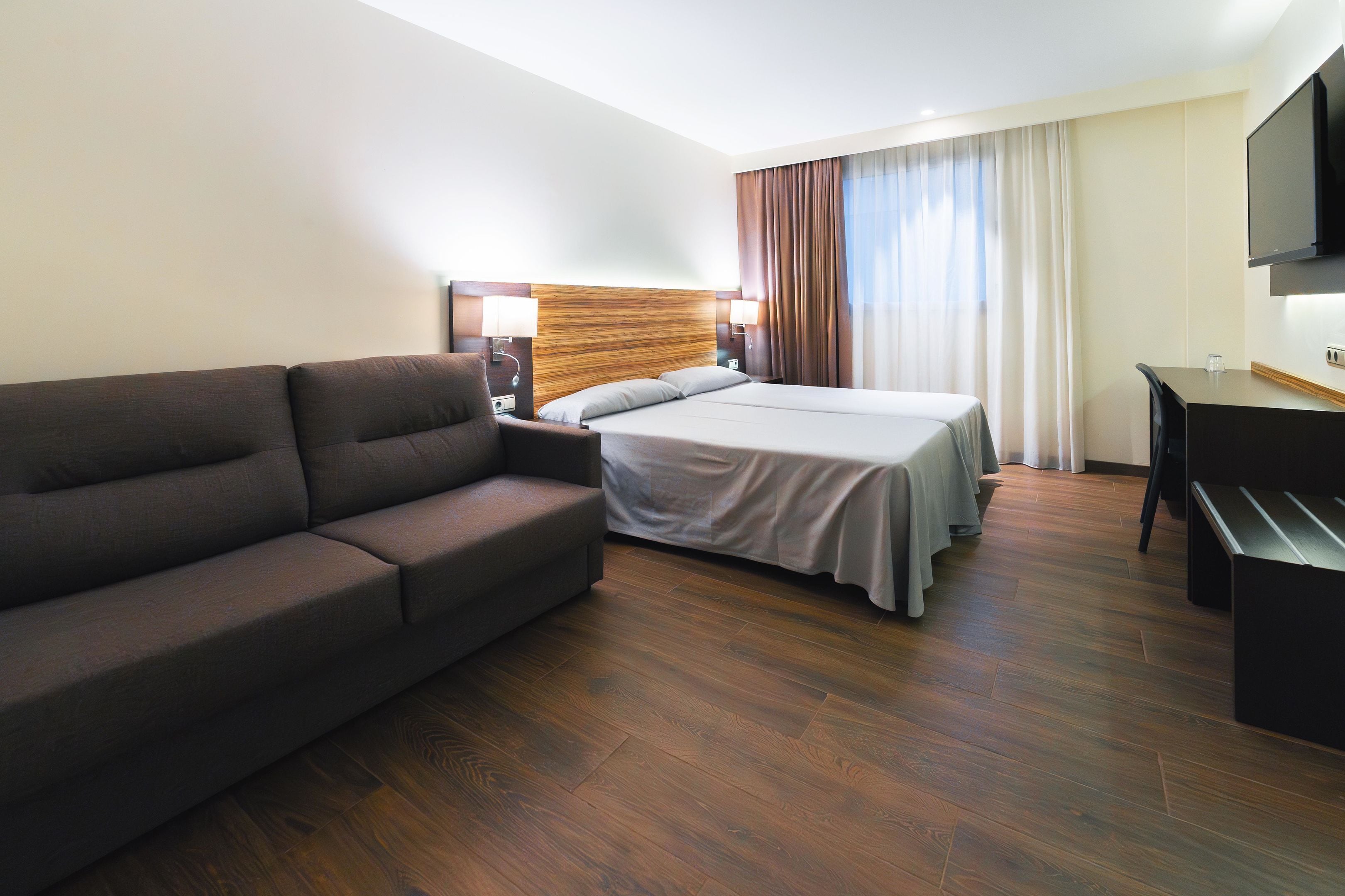 Una habitación de hotel con cama, sofá, escritorio y televisión.