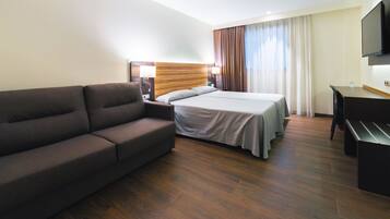 Una habitación de hotel con cama, sofá, escritorio y televisión.