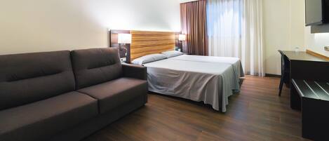 A hotel room with a bed, a sofa, a desk, and a TV.