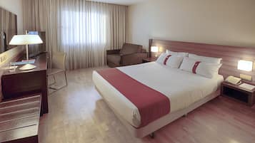 Una habitación de hotel con una cama grande, un escritorio con lámpara, una silla, un televisor y una mesita de noche con teléfono.