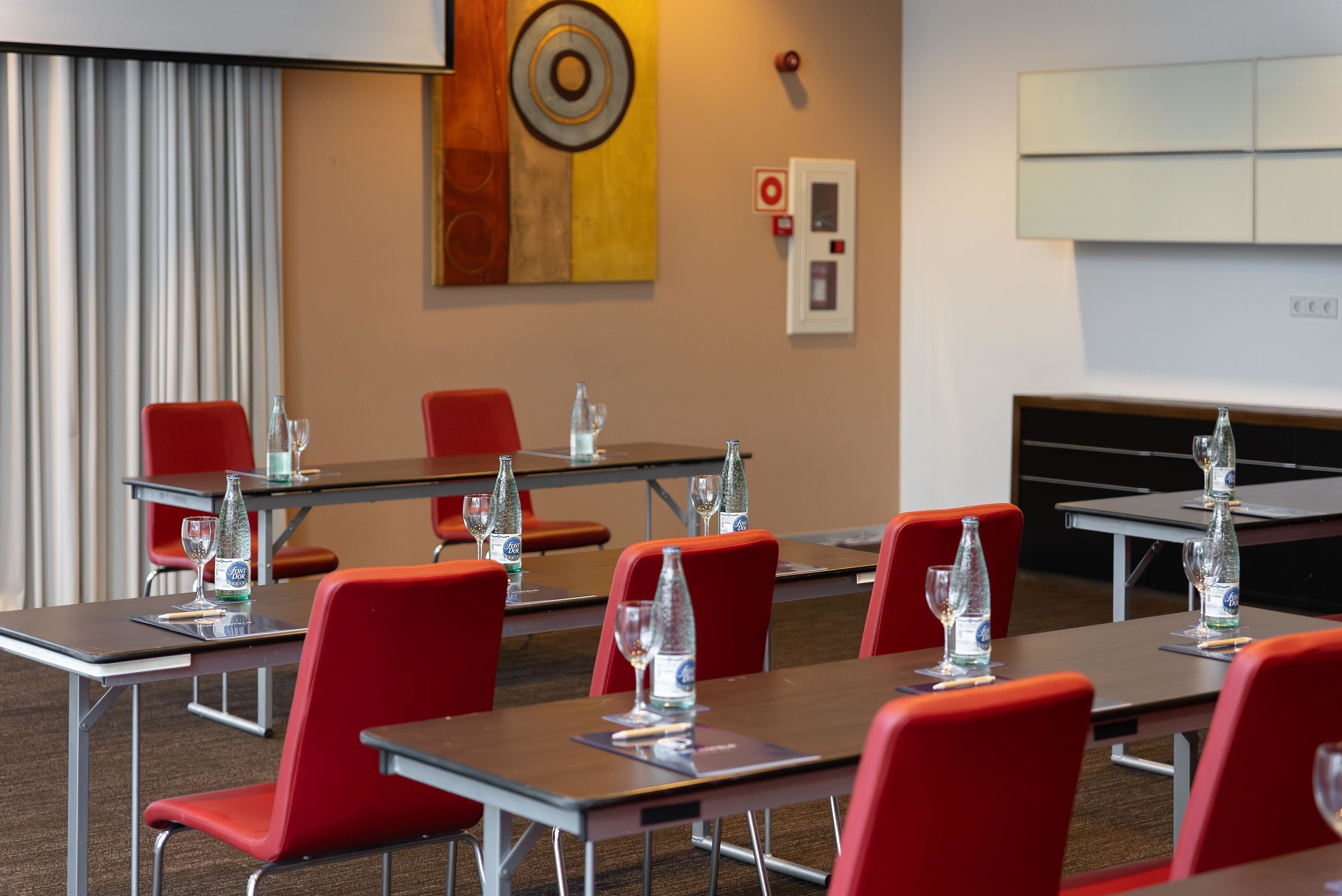 A conference room with red chairs and tables, equipped with water bottles and glasses.