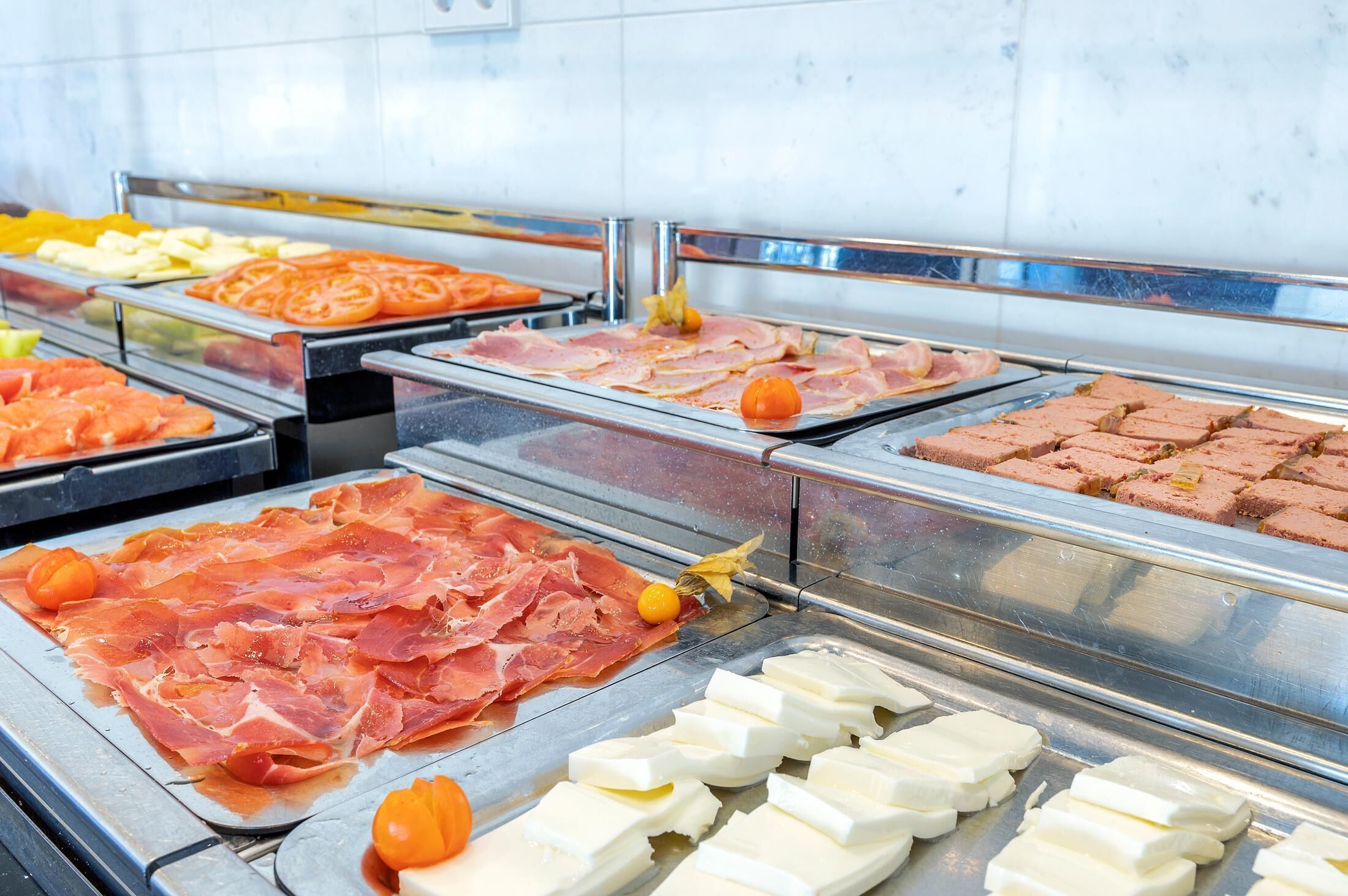 Un bufé con diversos alimentos, incluyendo carnes, quesos y frutas.
